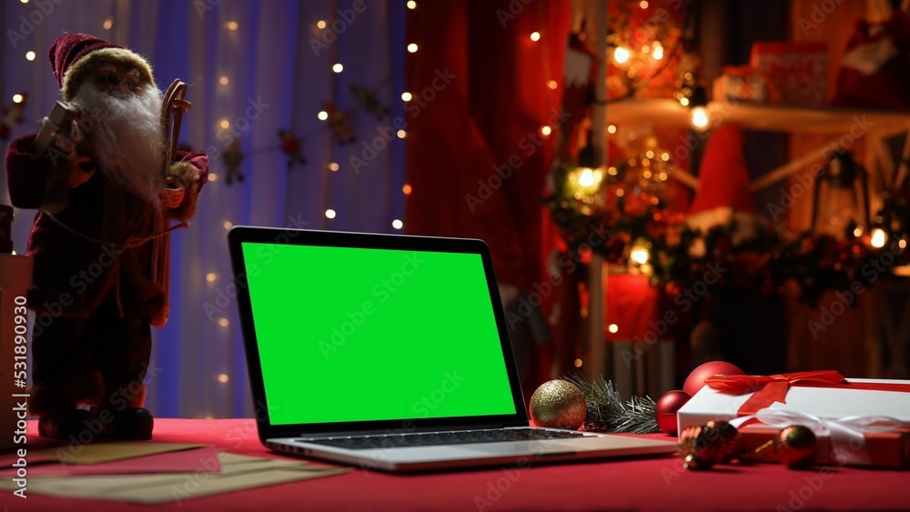 Green screen laptop standing on red table in room with christmas decorations. Place for advertising, New Year promotions. Chromakey notebook. Mockup monitor. Online shopping. Celebrating concept. Green screen laptop standing on red table in room with christmas decorations. Place for advertising, New Year promotions. Chromakey notebook. Mockup monitor. Online shopping. Celebrating concept.