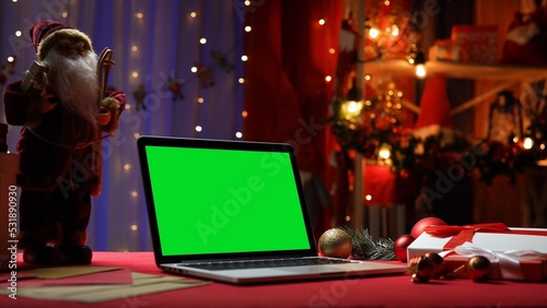 Green screen laptop standing on red table in room with christmas decorations. Place for advertising, New Year promotions. Chromakey notebook. Mockup monitor. Online shopping. Celebrating concept. © kinomaster