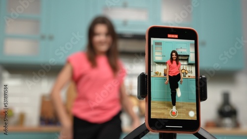 Young girl dancing and making videos for their blogs or social networks. Blogger filming vlog with trend content in kitchen. Online content, likes, stories, popularity, youth subculture. Close up. photo