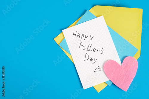 lettering happy father's day on paper, felt heart, postcard and envelope on blue background
