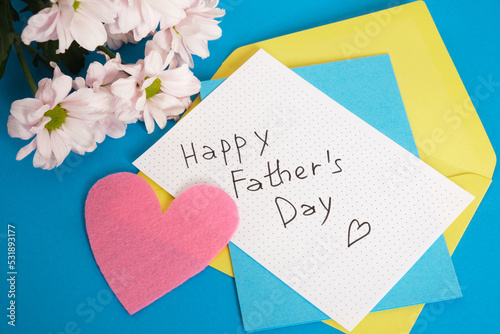happy father's day lettering on paper, flowers, postcard and envelope on blue background