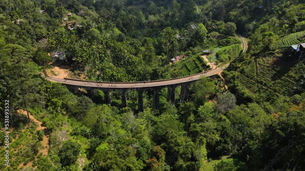 Several tourists walk across the Nine Arch Bridge in Sri Lanka among the green nature on a sunny day. High angle drone panning shot Several tourists walk across the Nine Arch Bridge in Sri Lanka among the green nature on a sunny day. High angle drone panning shot