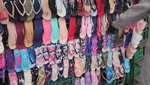 Video of a market stand rack with many types of women's sandals for sale. Camera tilts up, one person points at a specific sandal. Recorded in 4k quality in 60 fps. Market located in Lima, Peru. photo