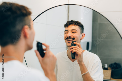 young adult man trimming hos mustaches in bathroom photo