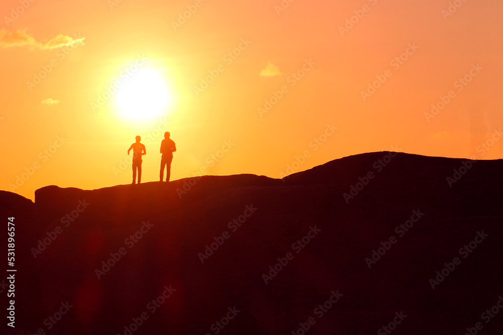 Silhouettes of two man against the setting sun. Two friends at sunset.