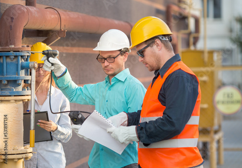 young men and a woman are standing near a gas pipe with an analyzer and documents. they are wearing helmets, glasses, gloves. checking for gas leaks..