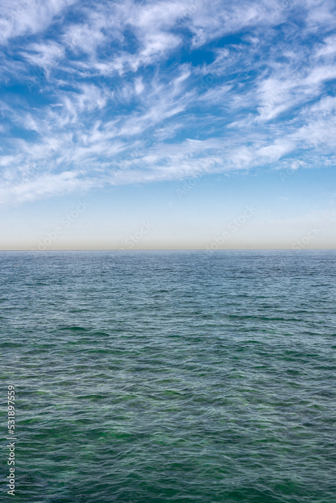 The surface of the sea under a cloudy blue sky. Blue-green wave surface of the sea going to the horizon. The surface of the sea under a cloudy blue sky. Blue-green wave surface of the sea going to the horizon.