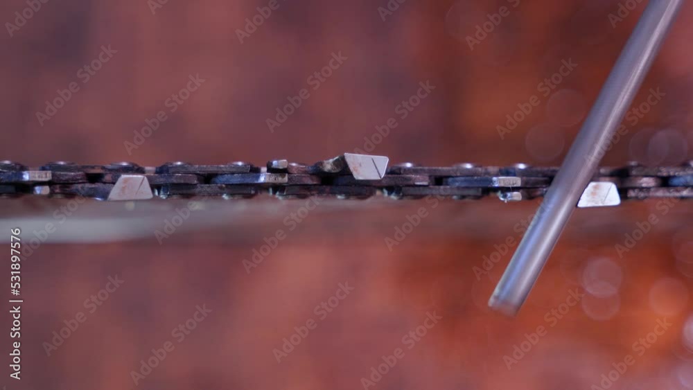 The process of sharpening chainsaw chain teeth with a round file close-up. Maintenance and preparation of the tool for work. Self repair saw on blurred background. Top view. The process of sharpening chainsaw chain teeth with a round file close-up. Maintenance and preparation of the tool for work. Self repair saw on blurred background. Top view.
