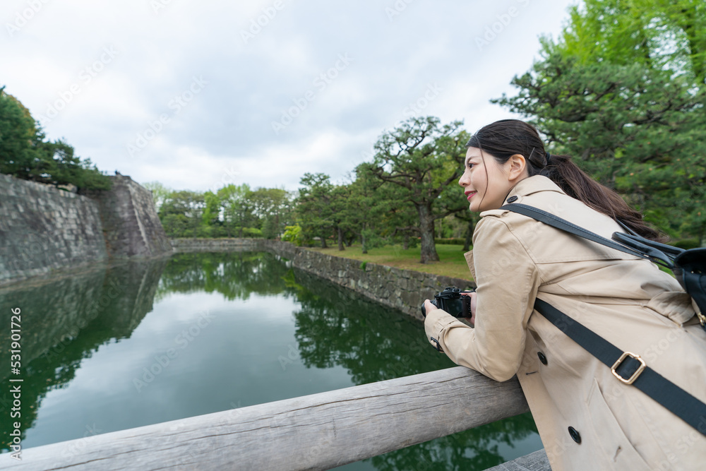 cheerful asian Japanese woman traveler leaning on wood bridge railing while appreciating historical inner moat at Motorikyu Nijyojo nijo castle in Kyoto japan