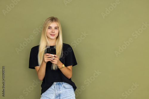 Young smiling happy woman hold in hand use mobile cell phone typing read message isolated on khaki background studio portrait. People lifestyle concept