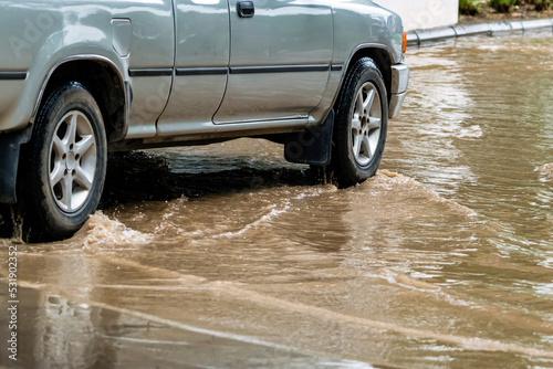 Pickup truck passing through flooded road. Driving car on flooded road during flood caused by torrential rains. Flooded city road with large puddle. Splash by car through flood water. Selective focus.