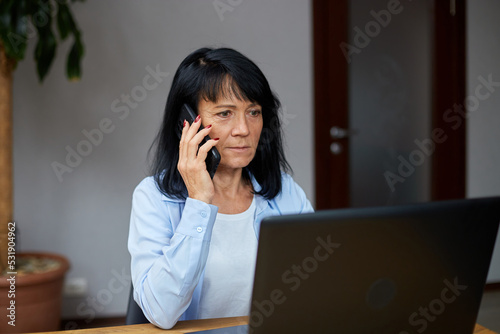 Senior woman talking speaking on phone on her workplace with laptop