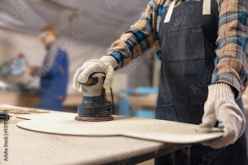 Closeup working of grinder on wood, woman carpenter performs work in protective clothing and respirator. Concept family business production furniture