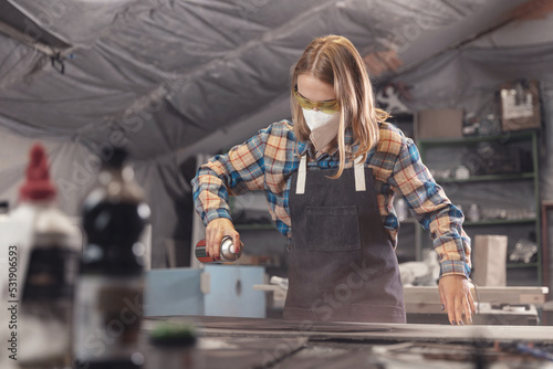 Foto Industrial worker carpenter woman performs painting of wooden detail in workshop
