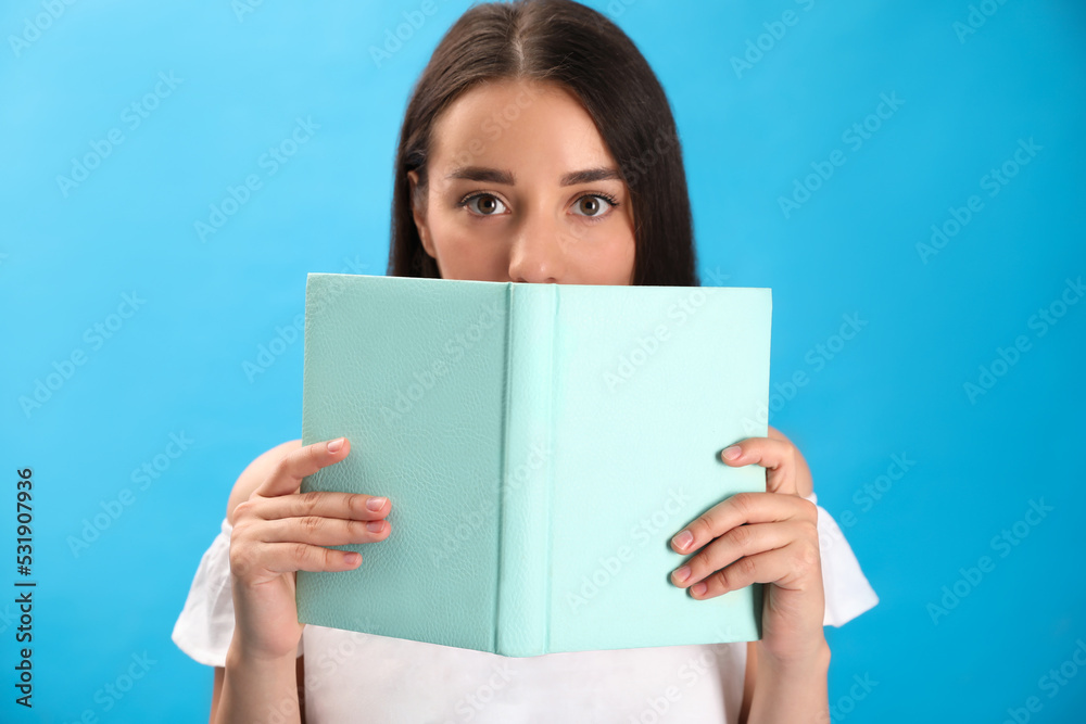 Beautiful young woman reading book on light blue background Beautiful young woman reading book on light blue background