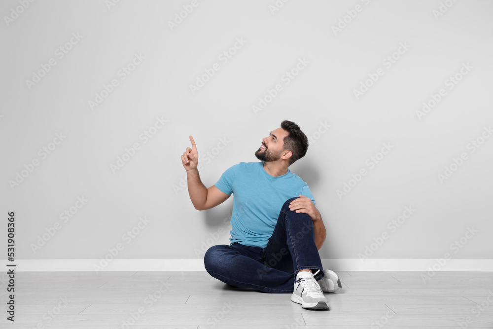 Young man sitting on floor near light grey wall indoors Young man sitting on floor near light grey wall indoors