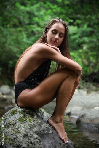 Beautiful young woman sitting on rock near mountain river outdoors