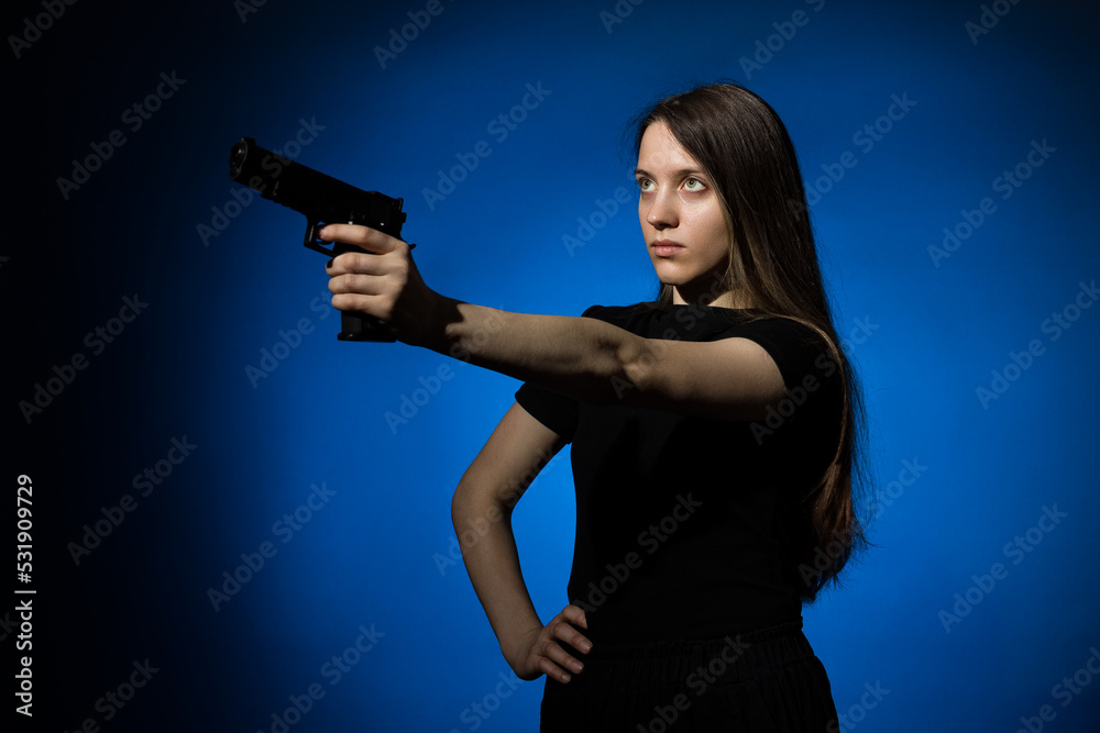 young beautiful woman with long hair in a black t-shirt aims a gun on a blue background young beautiful woman with long hair in a black t-shirt aims a gun on a blue background