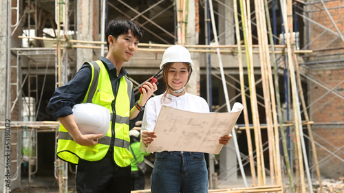 Architect team in safety helmet and reflective jacket standing front of construction site, working with blueprints