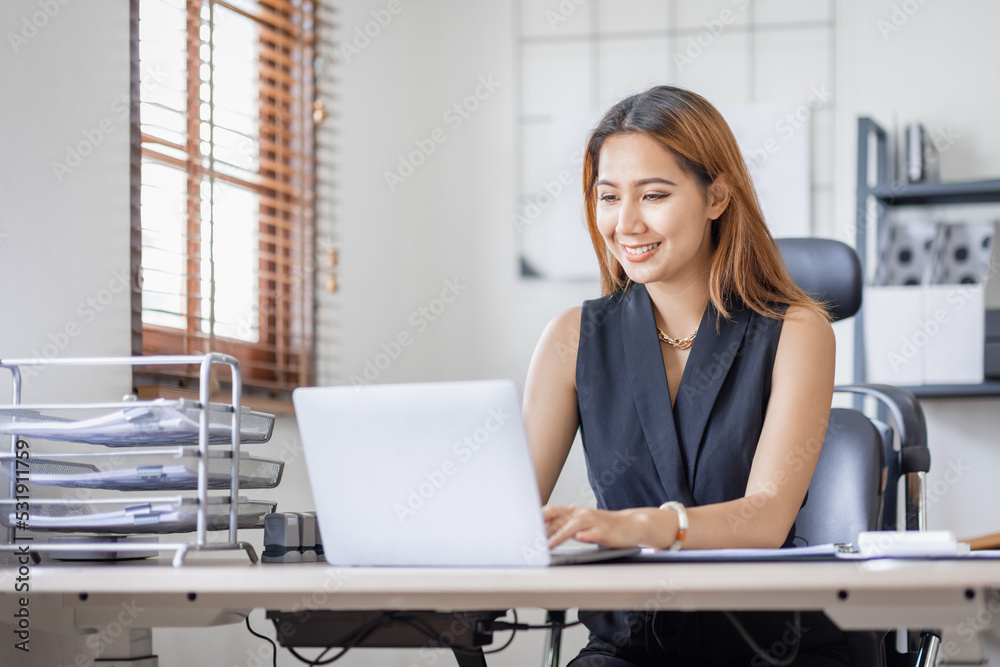 Young Asian female freelancer employee working at home workplace with laptop and papers on desk