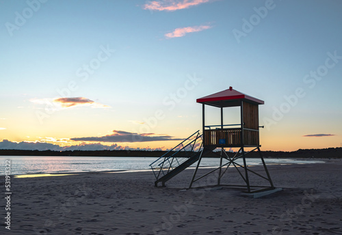 view of a red lifeguard deck on the shore of the sea at sunset time.