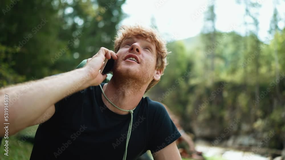 Happy tourist red haired man talking on phone while sitting near tent in the mountains Happy tourist red haired man talking on phone while sitting near tent in the mountains