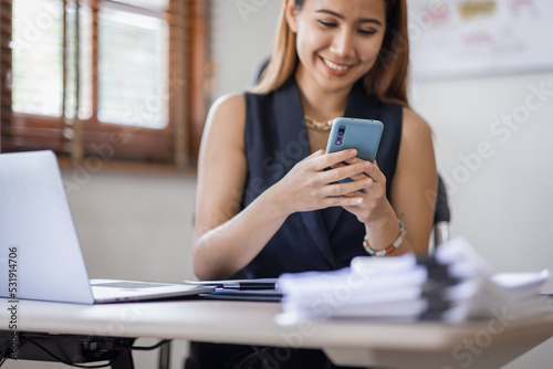 Happy Excited Asian young entrepreneur business woman using phone and laptop sitting on a desk at home workplace,