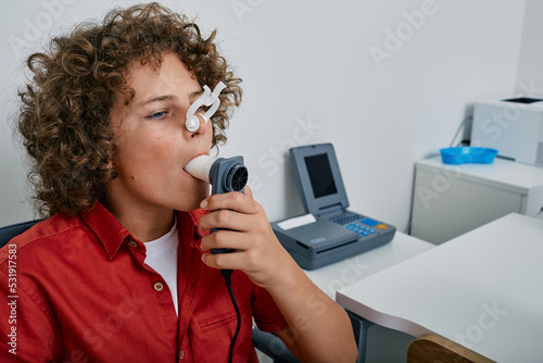Curly boy performing pulmonary function test and spirometry using spirometer at medical clinic. Spirometry of child's lungs