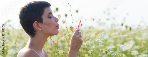 Valokuva Young woman blowing soap bubbles on the sunny summer meadow