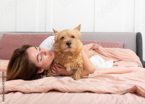 Young and beautiful woman lying in the bed and hugging her adorable pet dog. Perfect friendship concept