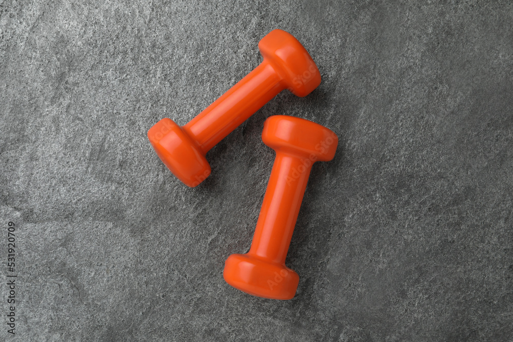 Two orange dumbbells on grey table, flat lay Two orange dumbbells on grey table, flat lay