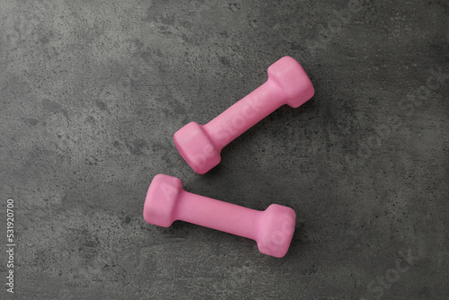 Two pink dumbbells on grey table, flat lay