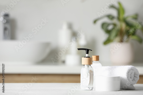 Different personal care products and rolled towel on white wooden table in bathroom. Space for text