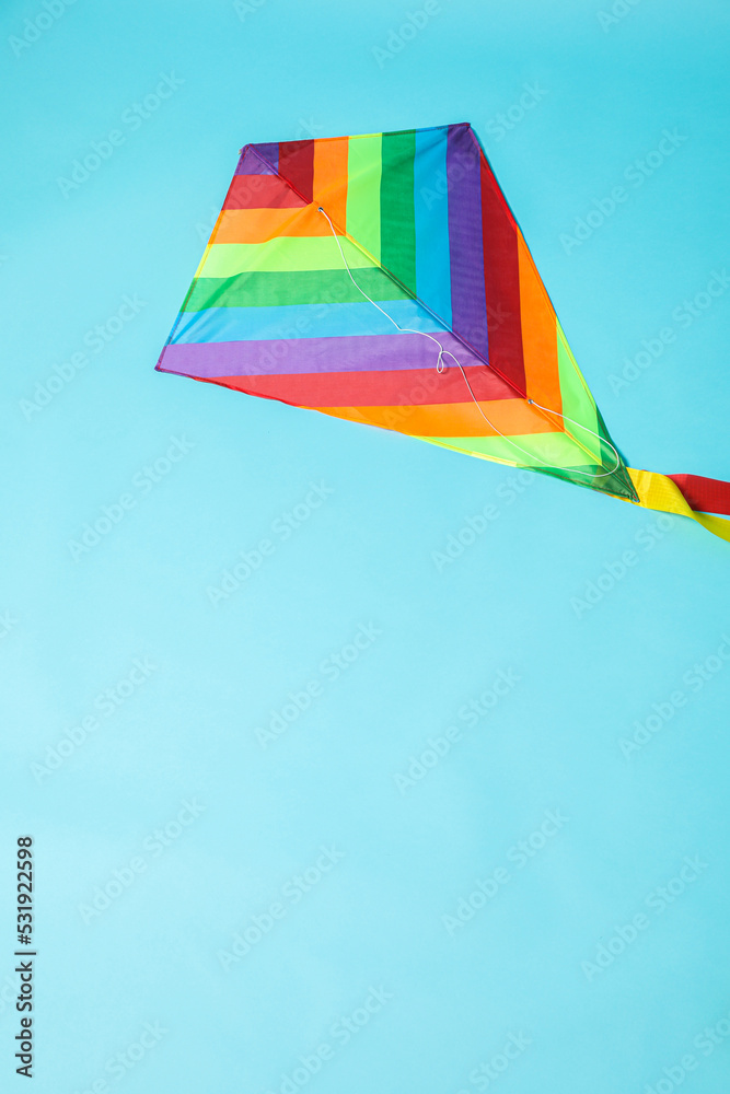 Bright rainbow kite on light blue background, top view. Space for text