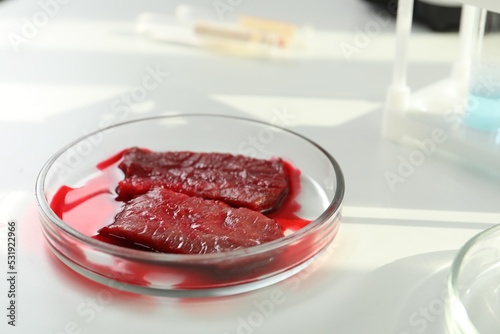 Petri dish with pieces of raw cultured meat on white table, closeup. Space for text