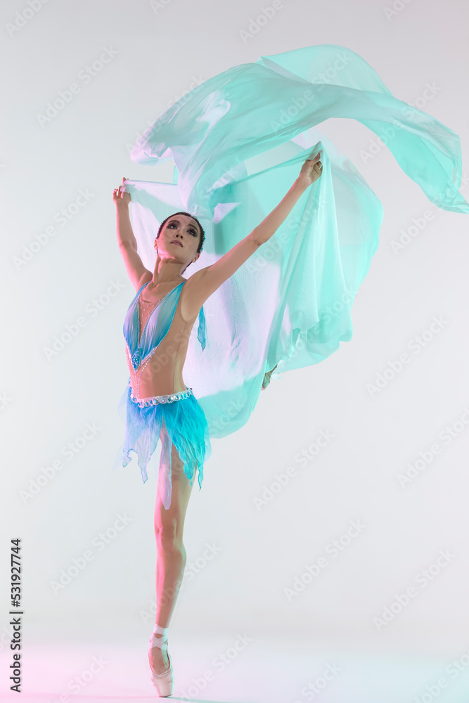 Dance Concepts. Professional Japanese Female Ballet Dancer Posing in Pale and Blue Dress With Flying Green Cloth In Hands Against White Dance Concepts. Professional Japanese Female Ballet Dancer Posing in Pale and Blue Dress With Flying Green Cloth In Hands Against White