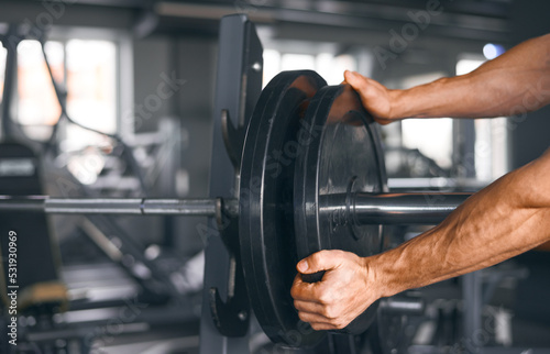 Strong male hands add weight plates to the barbell in the gym