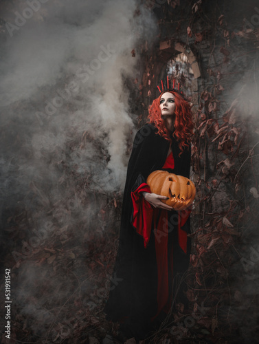 Fotografiet Red-haired beautiful woman in a gothic vintage black dress in a magical forest conjures