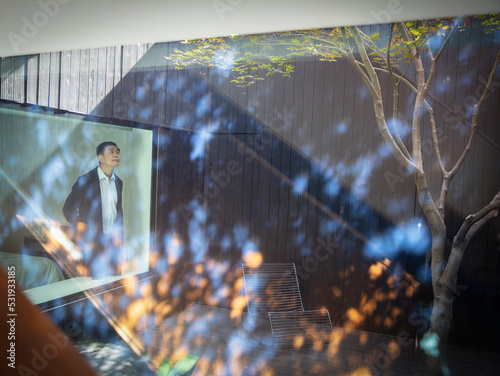 Man looking out bedroom window at sunny courtyard with tree photo