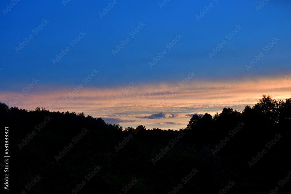 Close up on a dramatic sky in the afternoon with colorful clouds on the horizon spotted above a vast forest or moor in the middle of the summer seen on a Polish countryside from the top of a tall hill