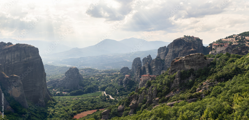 Obraz premium Aerial panoramic view over spectacular Thessaly plain landscape and byzantine monasteries of Meteora perched on sheer rocks, rays of the evening sun penetrate thick white clouds, Greece