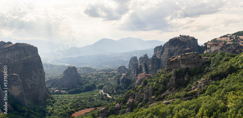 Aerial panoramic view over spectacular Thessaly plain landscape and byzantine monasteries of Meteora perched on sheer rocks  rays of the evening sun penetrate thick white clouds  Greece