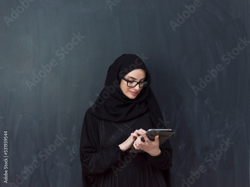 young modern muslim business woman using smartphone wearing sunglasses and hijab clothes in front of black chalkboard