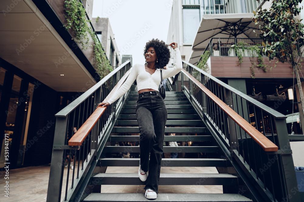 Young smiling african woman poses near stairs in the city