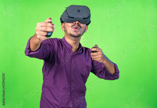 Excited young man with vr or virtual reality headset playing video game on metaverse using joystick on green screen background - concept of technology, entertainment and imagination