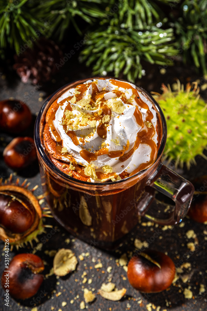 Glass cup with dark chestnut hot chocolate or choco latte, with whipped cream, caramel sauce and roasted chestnuts, over dark table copy space Glass cup with dark chestnut hot chocolate or choco latte, with whipped cream, caramel sauce and roasted chestnuts, over dark table copy space