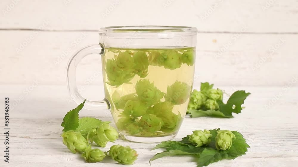 Herbal medicinal tea drink made of Humulus lupulus, the common hop or hops. Hops flowers with tea cup on white wood background, indoors home. Herbal medicinal tea drink made of Humulus lupulus, the common hop or hops. Hops flowers with tea cup on white wood background, indoors home.