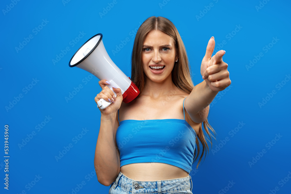 Young pretty woman with a megaphone against blue background in studio Young pretty woman with a megaphone against blue background in studio