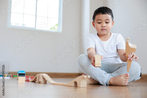 Attention asian boy playing wood block building rail way and road on the floor at home.