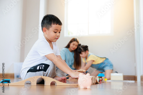 Cute asian boy playing wood block building rail way and road on the floor and his mother and sister help him to do that at home.